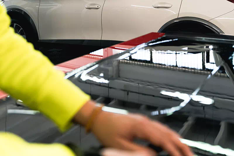 Dettaglio mano operatore che applica pellicola oscurante su auto.