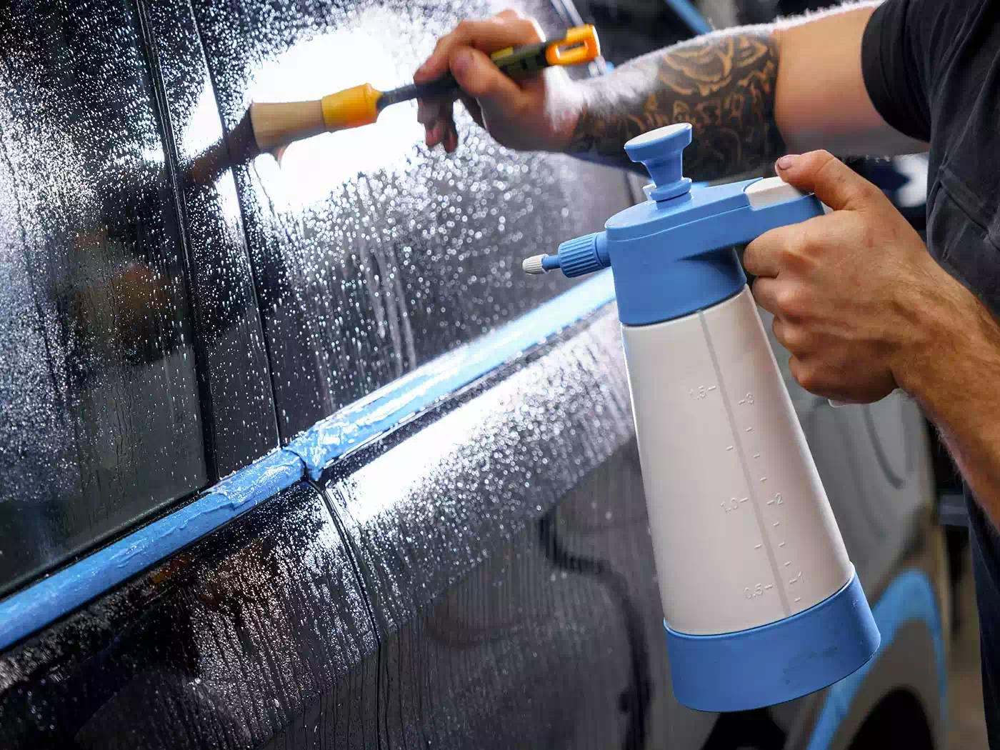 Dettaglio operatore mentre applica prodotto idrorepellente per il finestrino laterale dell’auto.