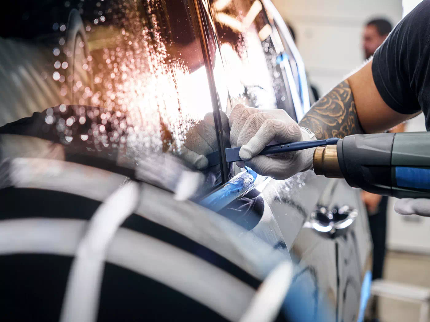 Dettaglio operatore mentre applica una pellicola idrorepellente per il finestrino laterale dell’auto.