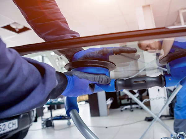 Dettaglio operatori che lavorano alla sostituzione del parabrezza rotto dell’auto.