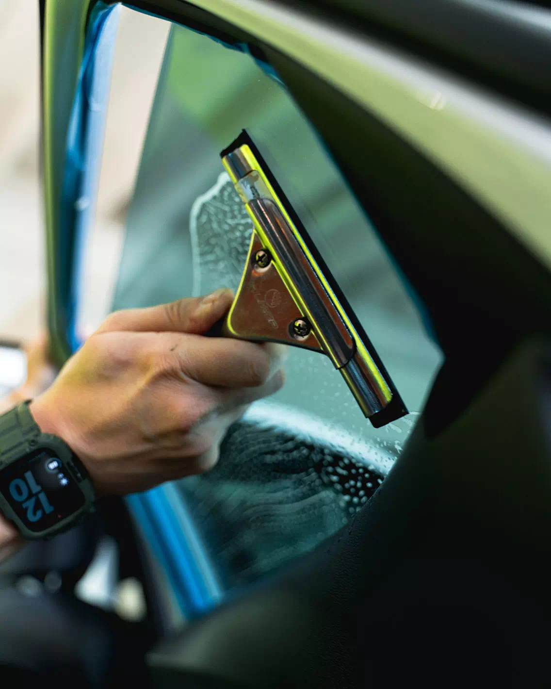 Mano di un operatore di Technoglass, attiva a Varese e Novara, pulisce vetro dopo aver applicato una pellicola oscurante.